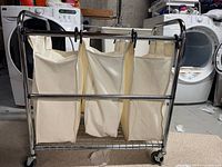 Front view of stainless steel laundry sorter with three canvas bags