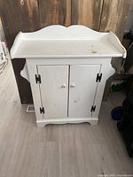 Front view of white solid pine cabinet with two doors and curved top edge showing minor stains and wear