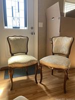 Two antique wood frame chairs with cream upholstery side by side in front of a door
