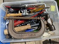 Plastic bin with assorted hand tools including large adjustable C-clamp, hammer, pliers, screwdriver and other tools.