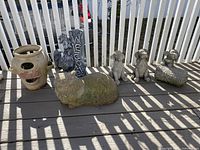 Photo of six concrete garden items displayed on deck including a planter, a sheep animal statue, three dog statues, and one dog statue with a welcome sign.