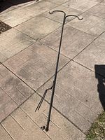 Full view of black metal double shepherd's hook plant hanger standing on paved surface outdoors.