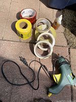 Photo showing the Mastercraft hot glue gun, multiple rolls of tape in red, yellow, white, and a bottle of adhesive glue all placed on outdoor stone surface.