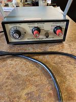 Front view of the Heathkit function generator showing frequency, frequency multiplier, and attenuation dials with power cable reflected.