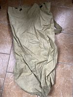 Top view of large olive green canvas duffel bag, showing metal eyelets along the opening and heavy creasing on the fabric.