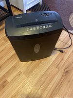Angled side view of Staples paper shredder showing the power cord, oval transparent window on the bin, and overall condition.