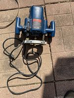Top view of the blue Ryobi plunge router with power cord on a stone patio surface.
