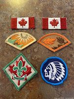 Six scout theme embroidered patches on a brown surface showing detailed designs and various shapes including rectangular, semi-circular, diamond, and circular.