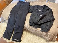 Black HJC Racing jacket and black Polaris bibbed snow pants laid out on bed to show full items
