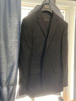 Black pinstripe men's suit jacket hanging on hanger with visible notch lapels and flap pockets.