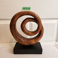 Front view of abstract wood sculpture displaying spiral loop design with smooth finish and mounted on black base. Approximate base width 12 inches indicated by label.