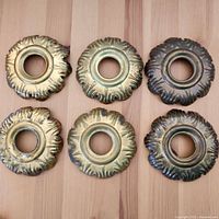 Top-down view of six brass bobeches with decorative scalloped edges and central hole for candles.