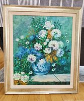 Framed canvas artwork showing a floral bouquet in a blue and white vase against a teal-green background.