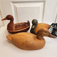 Photo showing three duck items: wicker basket, wood decoy, and glass lamp with cords visible.