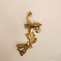 Front view of the wall shelf showing gold leaf finish and carved scroll and leaf details with two ledges for display.