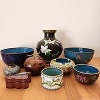 Nine cloisonne pieces arranged on a wooden surface, showing frontal view of patterns and shapes.