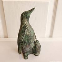 Front view of metal penguin mother and chick sculpture showing textured green patina and details of flippers and beak.
