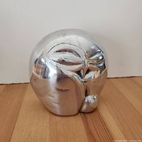 Front angle view of polished metal sleeping owl bookend showing detailed minimalistic eye and feather impressions.