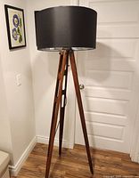 Full view of floor lamp showing wooden tripod base and black drum shade