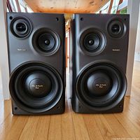 Pair of black Technics SB-CH737 3-way speakers shown from front standing on wooden floor.