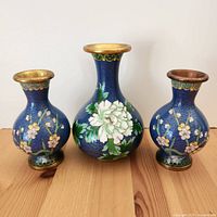 Three blue cloisonné vases on wooden surface showing floral designs and gold trim