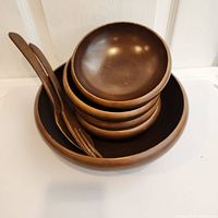 Stacked set showing the large bowl at the bottom, four small bowls nested inside, and two wooden serving utensils resting across the bowls.