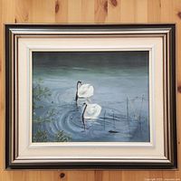 Full view of vintage framed oil painting depicting two swans on water with surrounding water plants and ripples.
