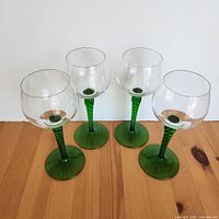 Top view of four vintage wine glasses showing clear bowls and green twirled stems on wooden surface.