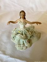 Front view of the porcelain lace figurine showing intricate green and white lace porcelain skirt and detailed upper body with arms extended.