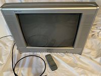 Full view of Electrohome 21-inch CRT television in silver and black color with connected power cable and remote control placed in front.