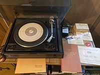 Photo of Garrard 72B turntable with tone arm, clear dust cover open, platter mat, and multiple manuals underneath.
