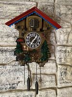 Front view of German style cuckoo clock hanging on stone wall showing detailed decoration, clock face, pinecone weights, and animated bird window.
