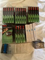 Green RCA T120 VHS videocassettes alongside white Memorex VHS tape boxes, Memorex C90 audio cassettes, and plastic cassette storage boxes on a white surface.