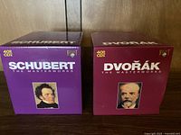 Photo of the two box sets side by side. Schubert box set in purple with portrait of Schubert and '40 CDX' label. Dvorak box set in maroon with portrait of Dvorak and '40 CDX' label.
