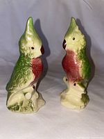 Front view of two ceramic bird figurines showing green and red coloration, standing upright.