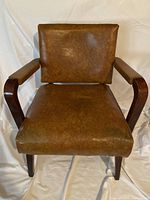 Front view of vintage armchair with brown pleather cushions and wooden armrests and legs