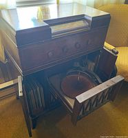 Wide angle view of vintage wooden console showing open doors revealing phonograph turntable and record storage compartments with vinyl records inside.