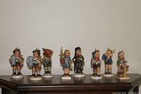 Eight 5.5 inch Hummel porcelain figurines arranged side by side on a wooden surface, showing detailed color and character of each figure.