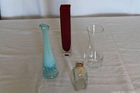 Four bud vases on a table: ruby-red and clear rectangular, blue opalescent hobnail, small clear pill bottle style, mid-sized clear glass vase.
