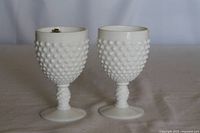 Front view of two white hobnail milk glass goblets set together