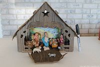 Front view of the 10 inch cardboard stable with resin nativity figures inside, including Mary, Joseph, baby Jesus, angel, and animals. A black marker pen is placed to the side for scale reference.