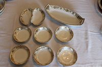 Eight Noritake China pieces including a divided relish dish, celery/asparagus dish, and six small fruit bowls, all with Christmas Ball pattern and gold trim.
