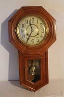 Photo of D&A regulator pendulum wall clock with wooden octagon frame and visible brass pendulum.