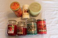 Seven assorted scented candles displayed on white surface showing brand labels and colors.