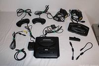 Full lot layout including Sega Genesis console, four controllers, power supply, AV cable, two games, cartridge adapter, and smaller connectors.
