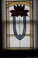 Framed stained glass window panel with lotus flower design, shown against window blinds for lighting contrast.