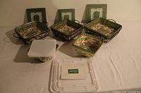 Full view of the 16 piece Temptations serving ware set including 3 ceramic dishes in wrought iron baskets with lids and trivets, 2 mixing bowls with lids, and plastic storage lids.