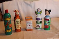 Five baby product containers arranged in a row, featuring Tigger, Buzz Lightyear, and Mickey Mouse characters, alongside a metal tin baby powder container.