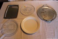 Wide view of all five serving platters and trays on a beige tablecloth, showing the Rodney Kent tray, Moonstone glass dishes, William Adams crystal platter, white ceramic platter, and silver metal tray.