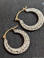 Two 10KT gold hoop earrings with cubic zirconia stones visible on a black background, showing front side with stones.